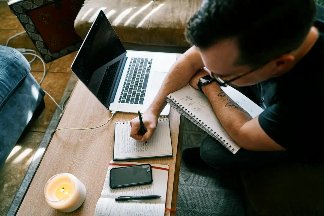 A man writing in a notebook beside a laptop, the way to weigh an IPTV provider such as TvNado before ordering